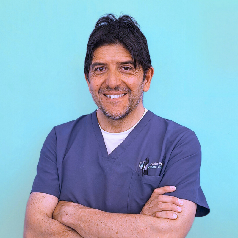 Il Dottor Gian Luigi Vannucci, co-fondatore della Clinica Veterinaria Costa d'Argento e direttore sanitario dell'Ambulatorio con sede a Manciano. Un uomo che indossa un camice medico blu scuro si staglia su uno sfondo blu chiaro, sorridendo con le braccia incrociate.